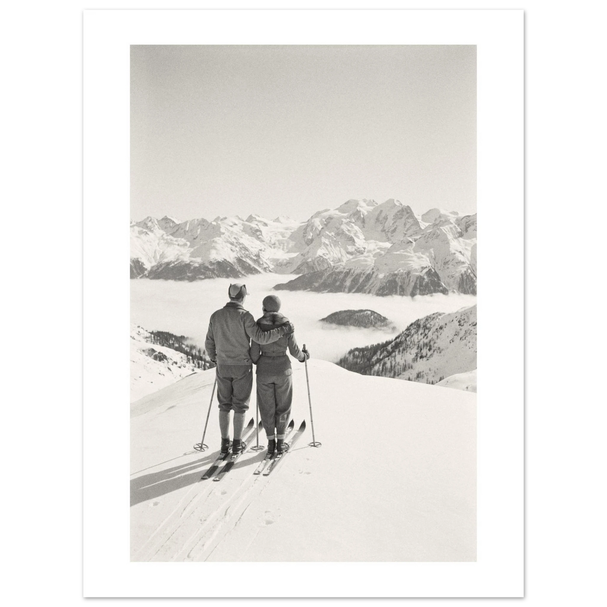 Ski couple resting on a snowy alpine summit with skis planted, looking over a range of peaks, 1932 style black and white photo print